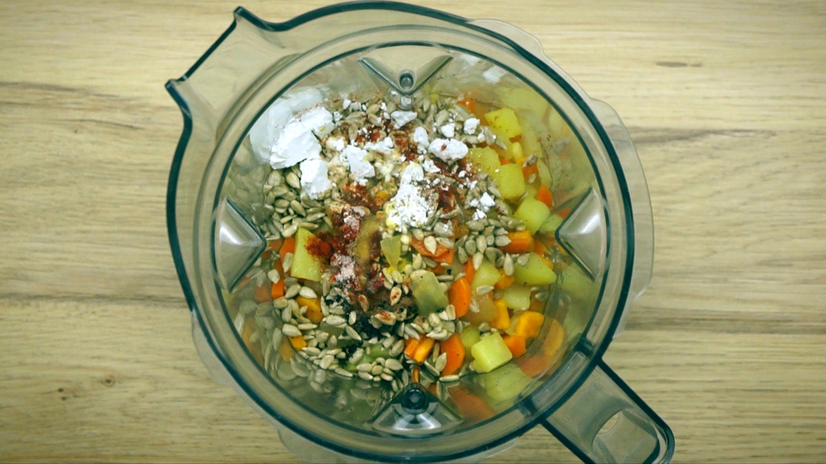 Blender with cooked diced carrots, potatoes, orange sweet potatoes, onions, garlic, sunflower seeds, paprika powder, and white corn starch.