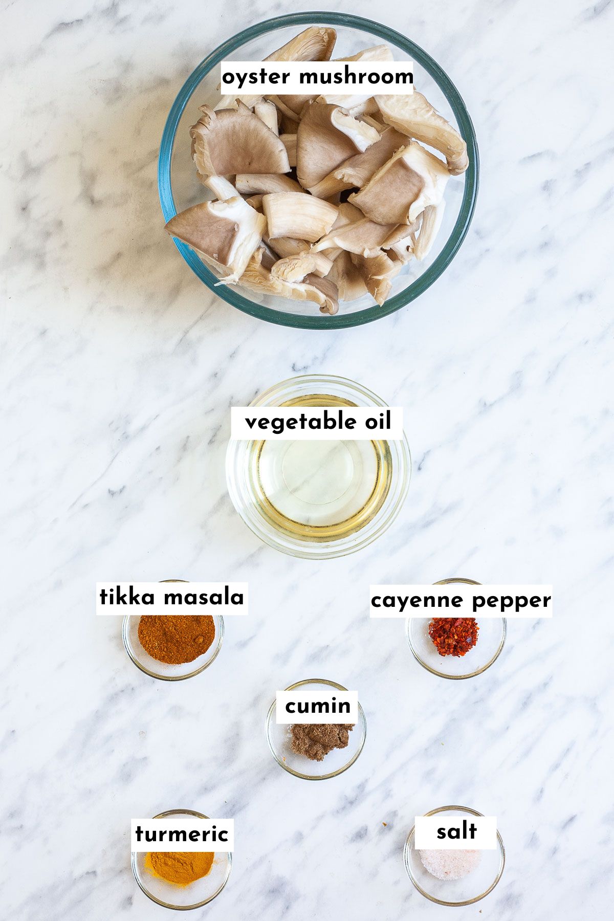 Ingredients of mushroom tikka masala placed in small glass bowls: mushrooms, oil, different brown and yellow spices.