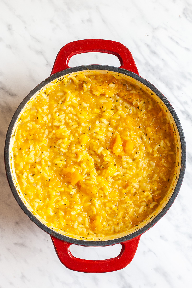 Red white cast iron skillet with orange risotto.