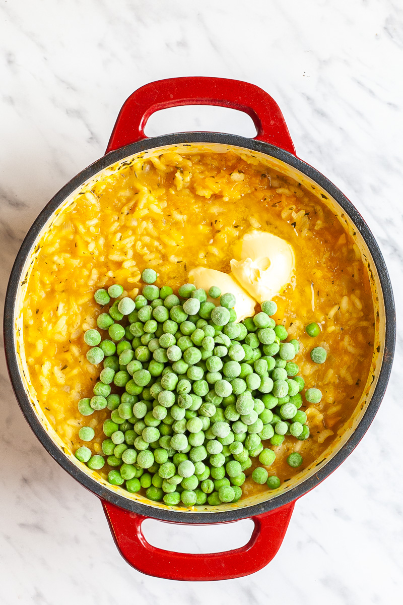 Red white cast iron skillet with orange risotto topped with frozen green peas. 