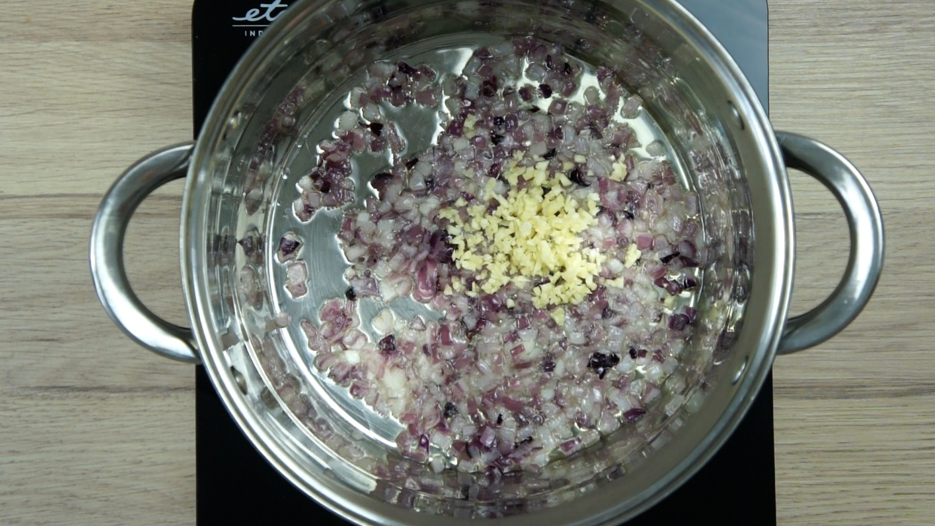 Purple diced onion in stockpot with a heap of minced garlic. 