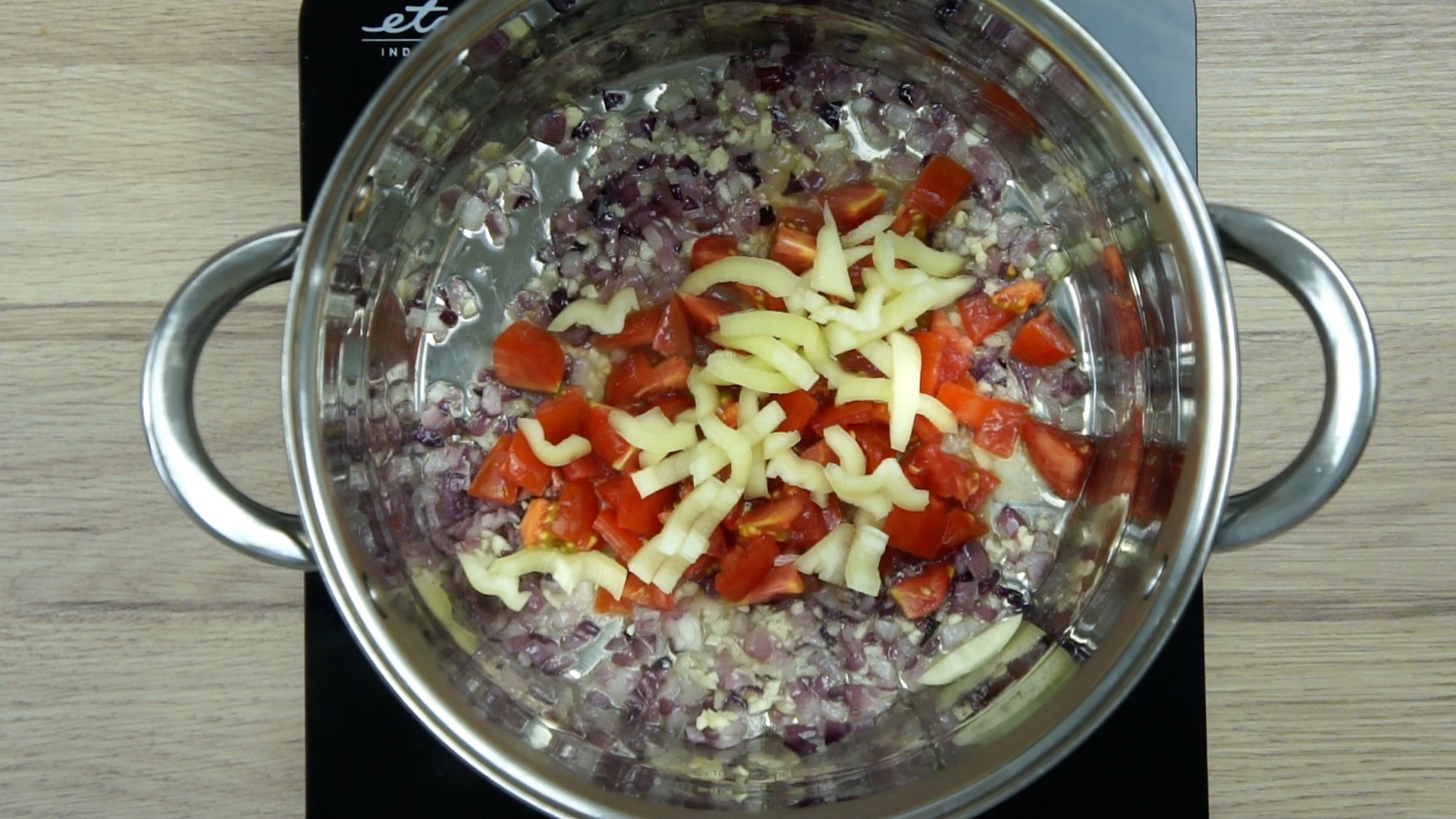 Purple diced onion in stockpot with tomato and yellow pepper slices.