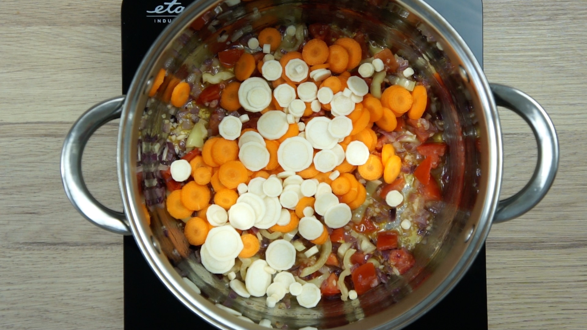 Purple diced onion in stockpot with tomato and yellow pepper slices and carrot slices.