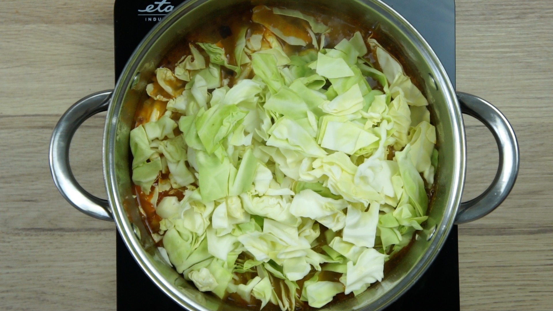 Brown soup in a stockpot topped with fresh cabbage leaves.