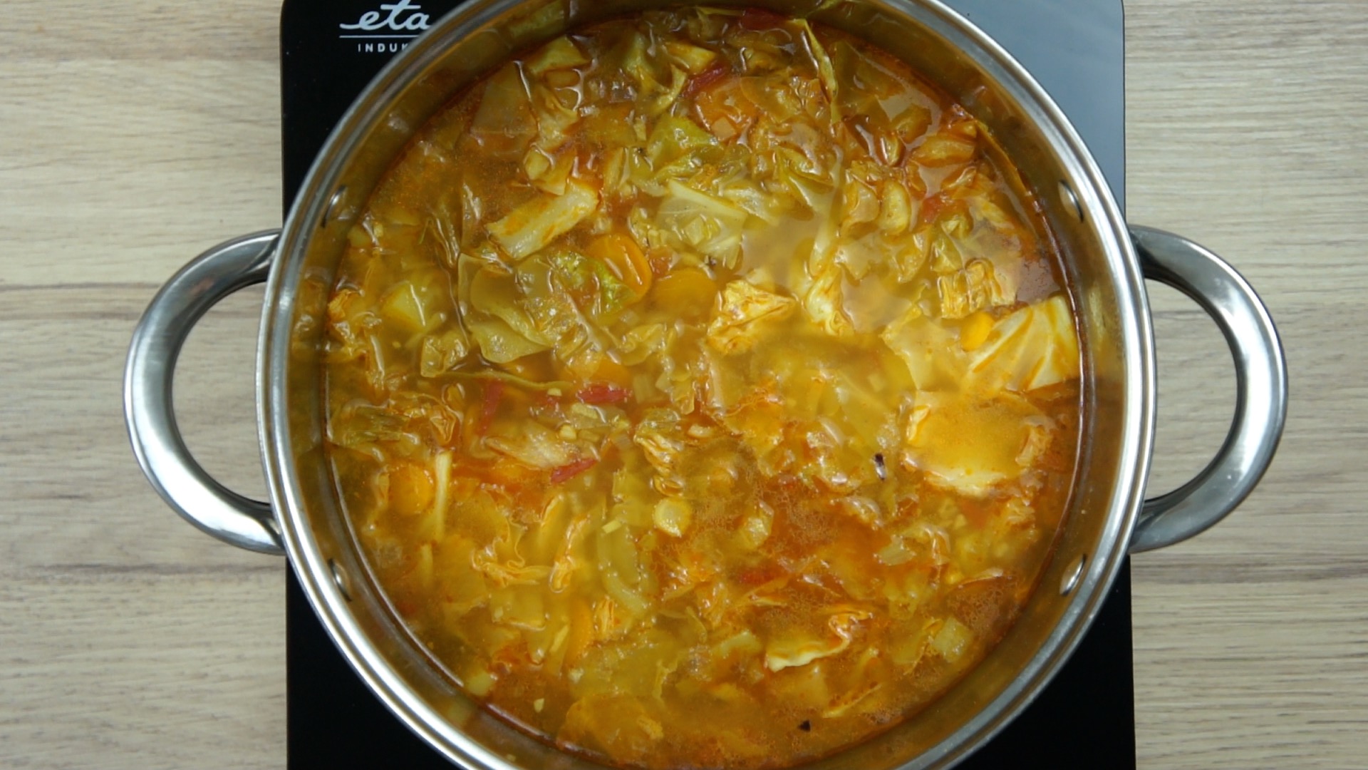 Brown soup with cabbage leaves and other vegetables in a stockpot.