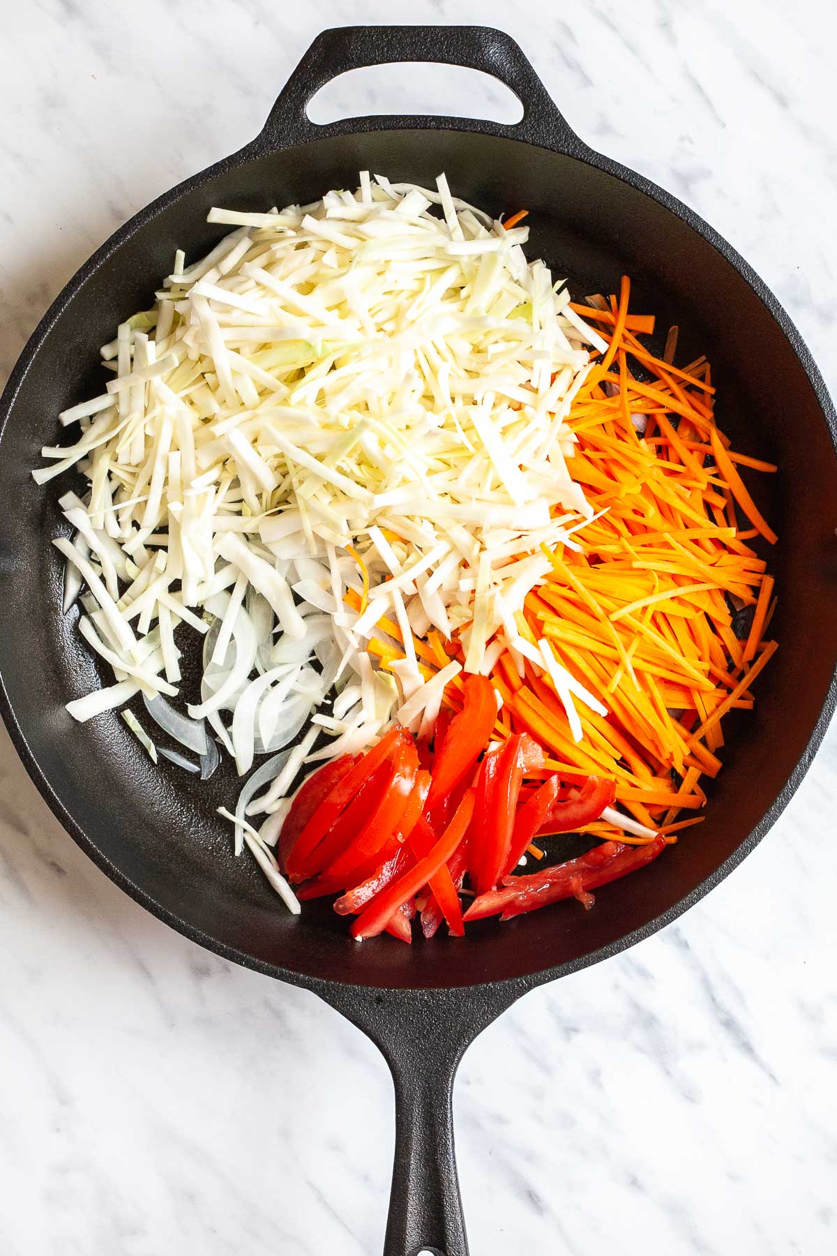 Cast iron skillet with sliced onion, cabbage, tomatoes, and carrots.