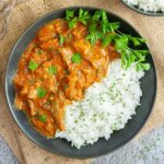Large black plate with white rice and mushroom shreds in orange thick sauce sprinkled with chopped green herbs and a twig of parsley on top.