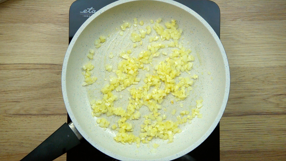 White frying pan with chopped onion in oil