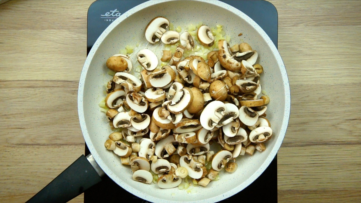 White frying pan with raw mushroom slices.
