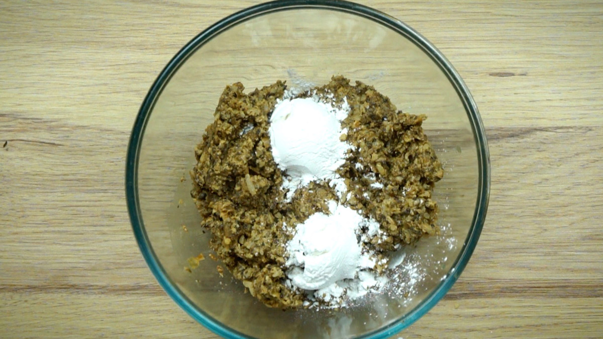 A glass bowl with brown puree and white flour. Mushroom and onion pieces are still visible.