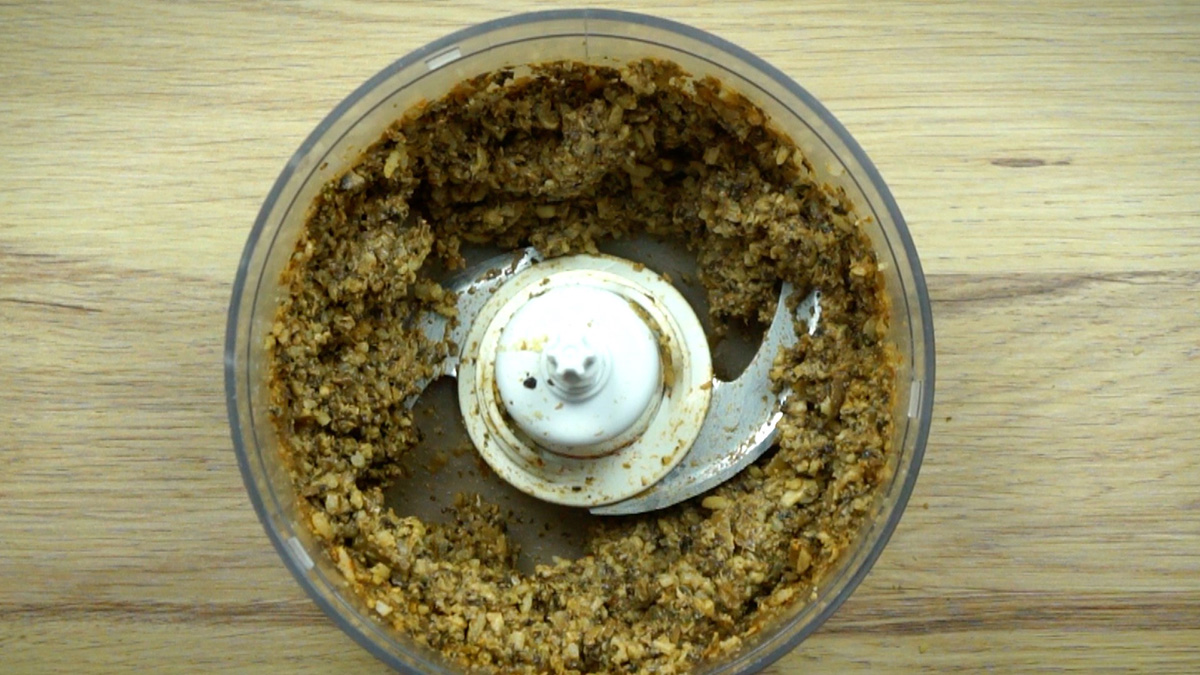 Food processor with dark brown puree. Mushroom and onion pieces are still visible.