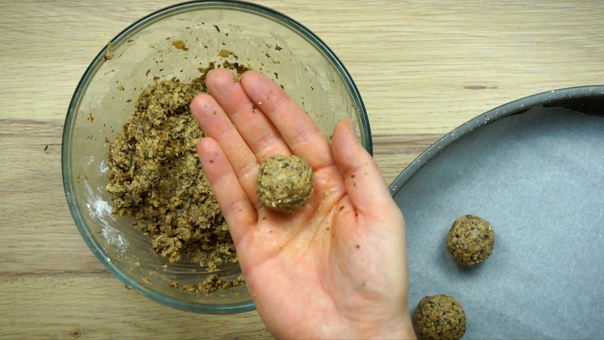 A hand is holding a small brown ball above a glass bowl of the mixture.