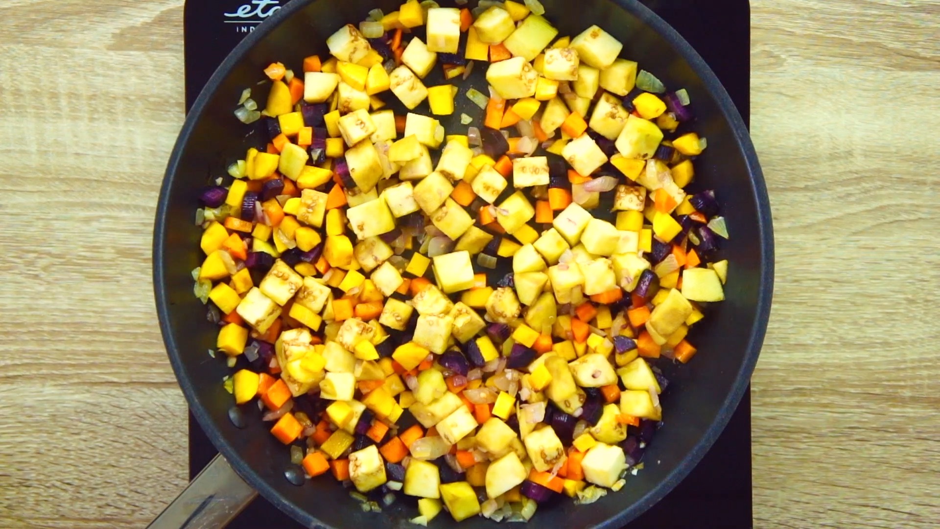 Black frying pan with lots of colorful diced vegetables like eggplant, zucchini, carrots. 
