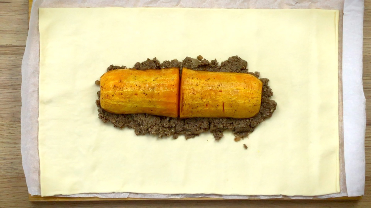 Yellow puff pasty with a large heap of thick green paste and two halves of a butternut squash neck on top in the middle.