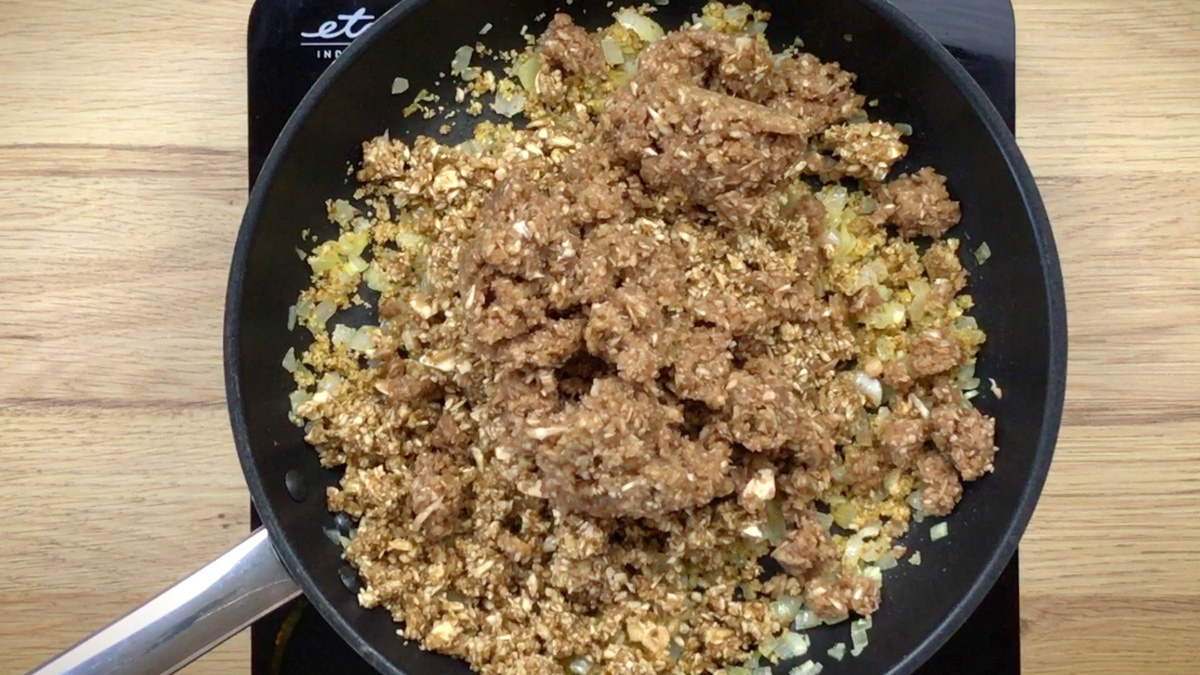 Black frying pan with minced onion and garlic with a large heap of finely minced mushroom and walnut