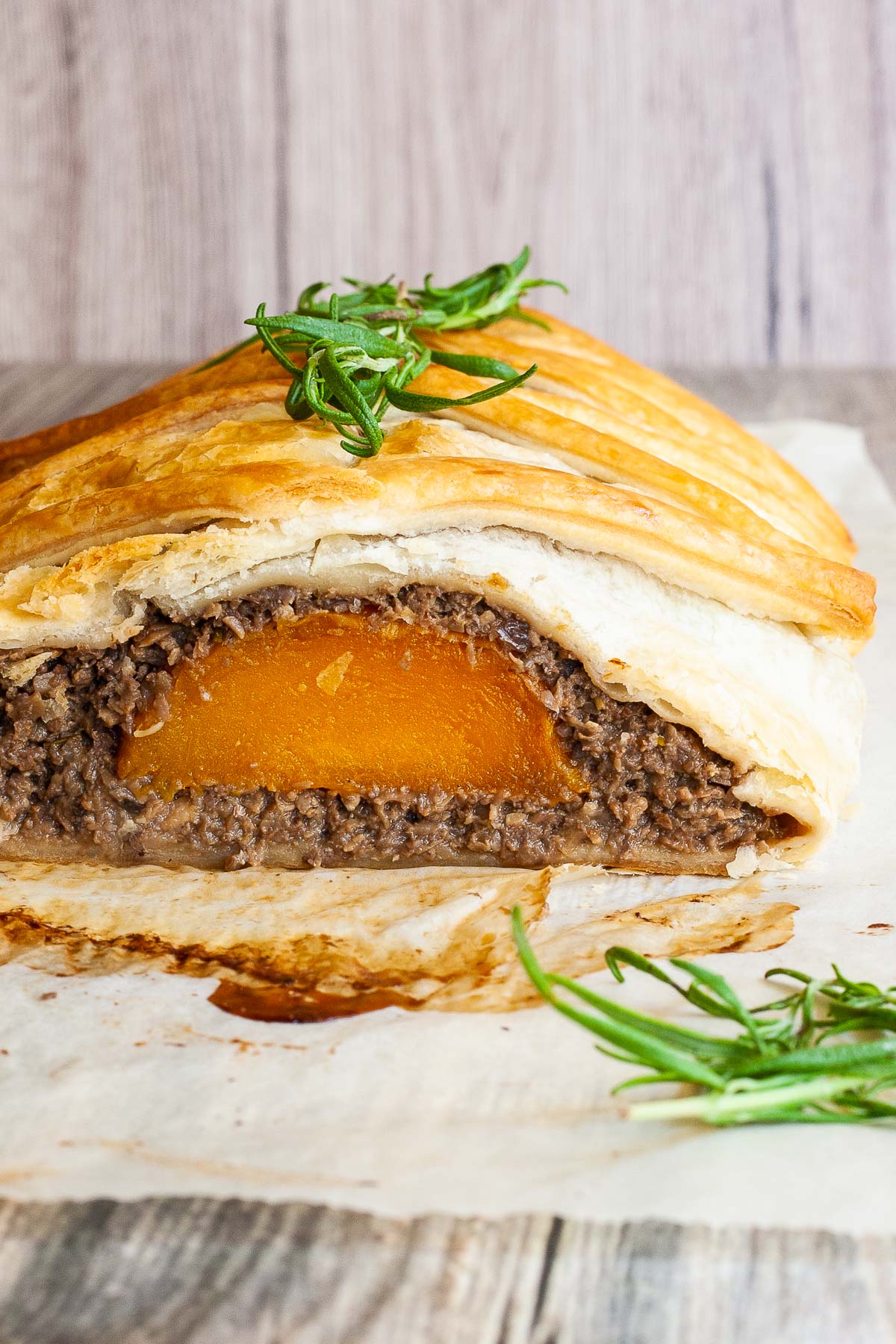 A slice of wellington real close showing yellow squash slice in the middle and brown puree around wrapped in a pastry shell. Green herb leaves on top.