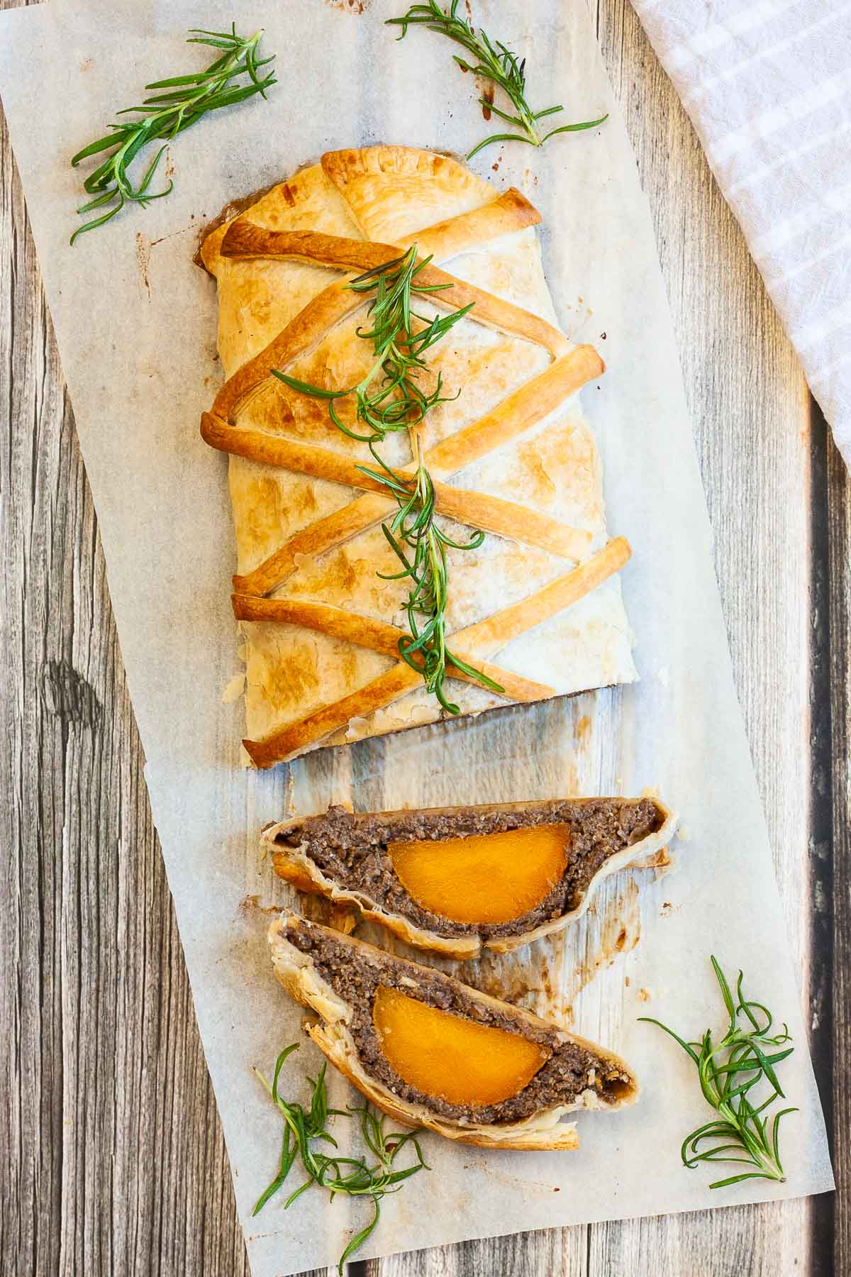 2 slices of vegan wellington on the side. Yellow squash with brown puree around wrapped in a pastry shell. Green herbs are around.