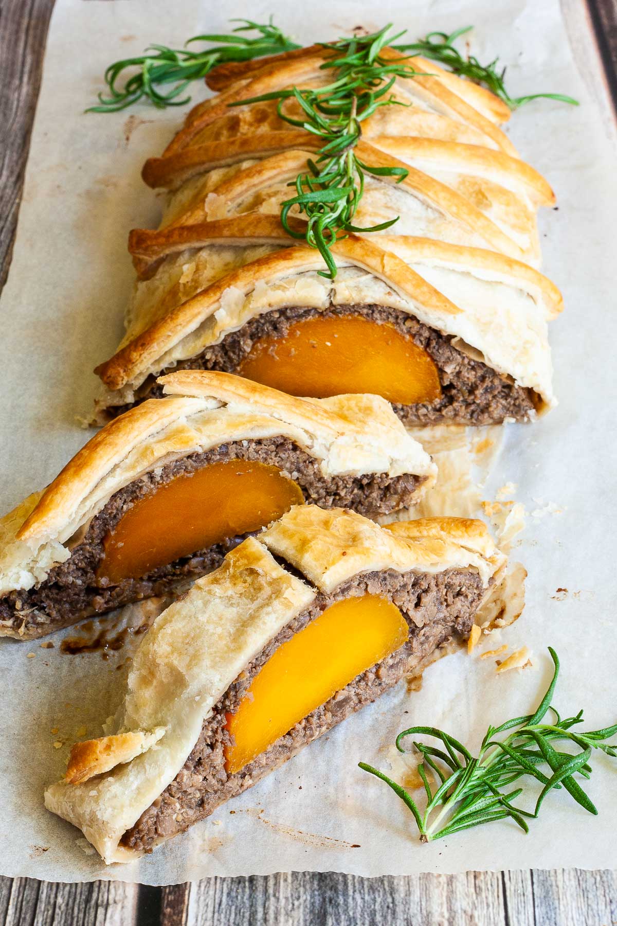 2 slices of vegan wellington on the side. Yellow squash with brown puree around wrapped in a pastry shell. Green herbs are around.