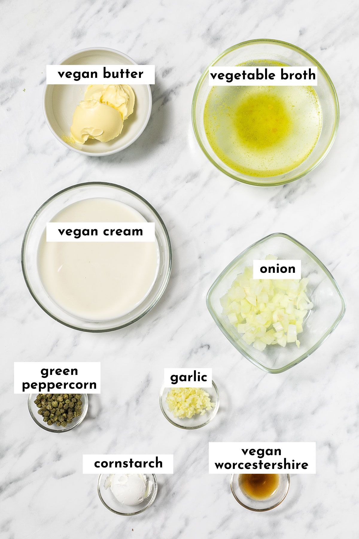 Ingredients of vegan green peppercorn sauce in small glass bowls like butter, vegetable broth, cream, chopped onion and garlic, whole peppercorns, starch and dark brown worcestershire sauce