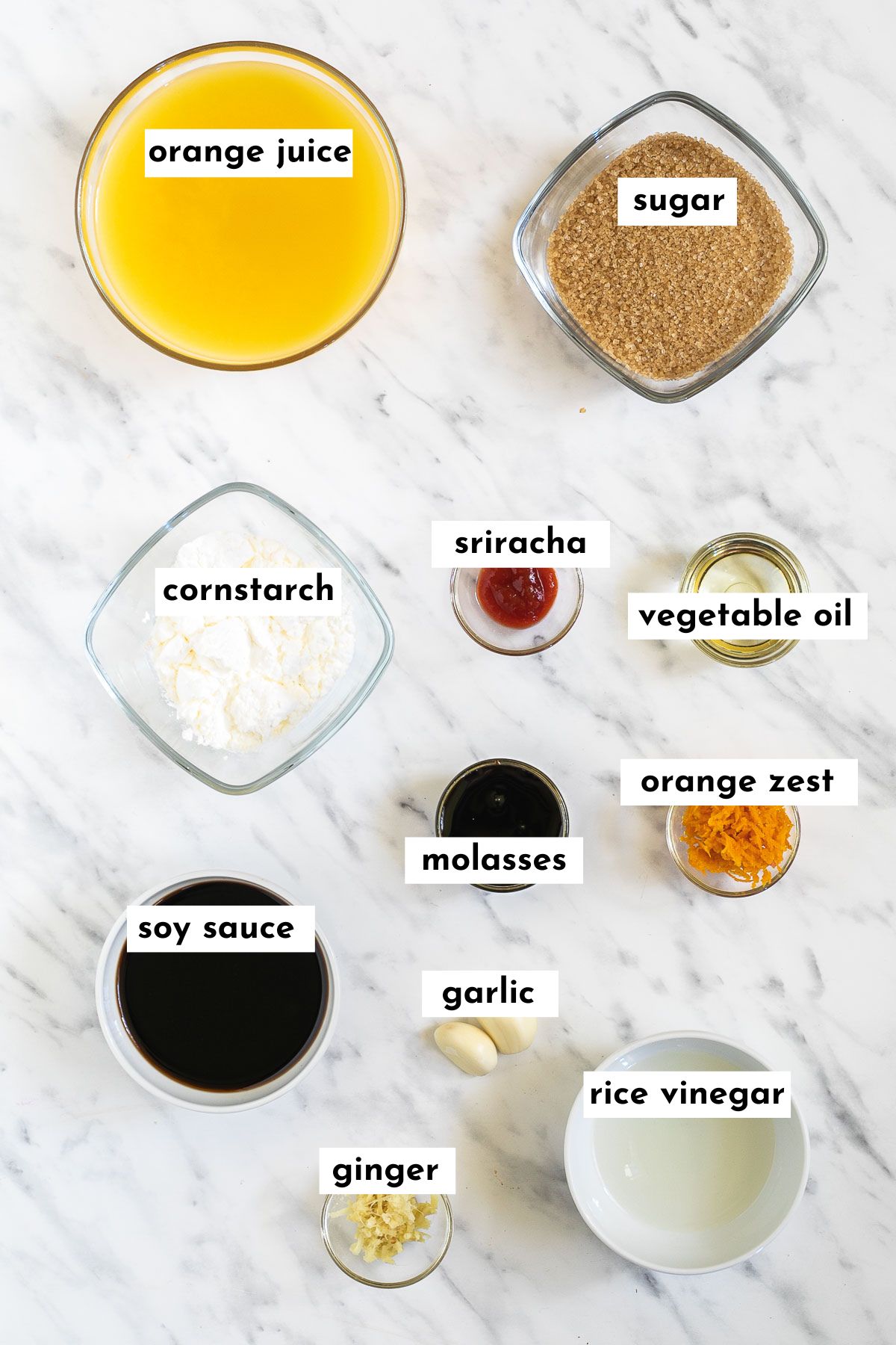Ingredients of orange tofu are in small glass bowls like orange juice, sugar, corn starch, molasses, soy sauce, orange zest, oil, vinegar and garlic, ginger.
