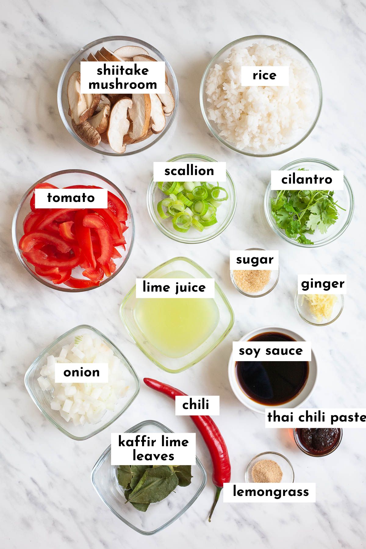 Ingredients of tom yum fried rice in small glass containers like sliced mushrooms, rice, tomato, scallion, cilantro leaves, chopped onion, ginger, lime juice, chili, kaffir lime leaves, soy sauce and chili paste