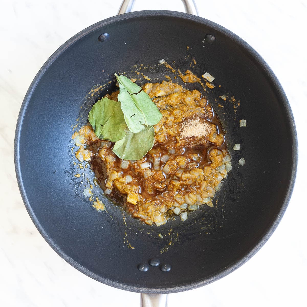 Wok with finely chopped onion in green-brown paste with green kaffir lime leaves, black sauce, and sugar added on top. 