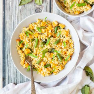 2 white bowls with fried rice in an orange sauce with sweet potato cubes and green bean pieces, A fork is placed inside the dish.