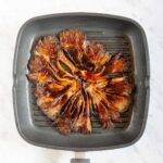 Black grill pan from above with crispy dark brown juicy flattened oyster mushroom clusters