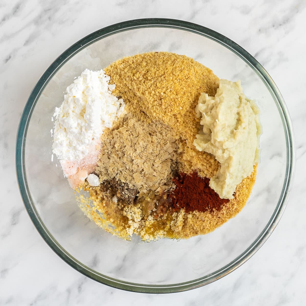 A large glass bowl with different spices and ingredients to make the tofu burger.