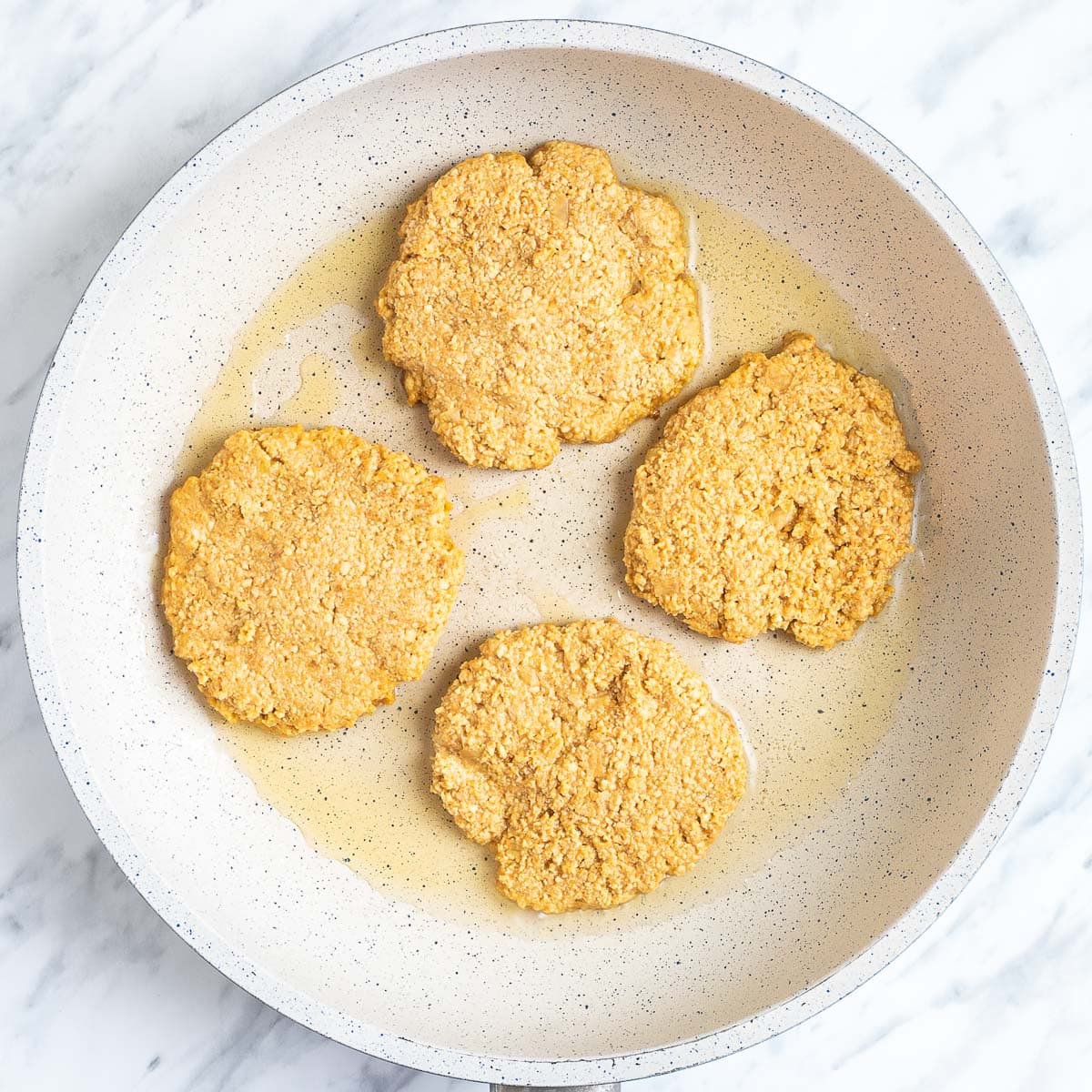 4 raw burger patties are in a white frying pan.