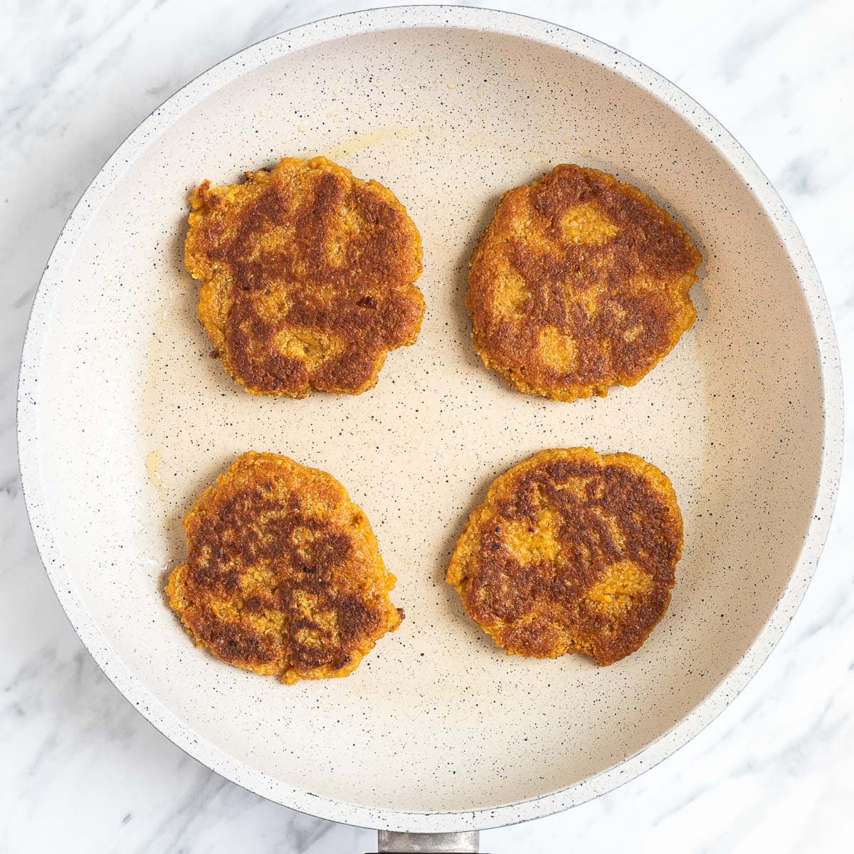 4 golden brown burger patties in a white frying pan.