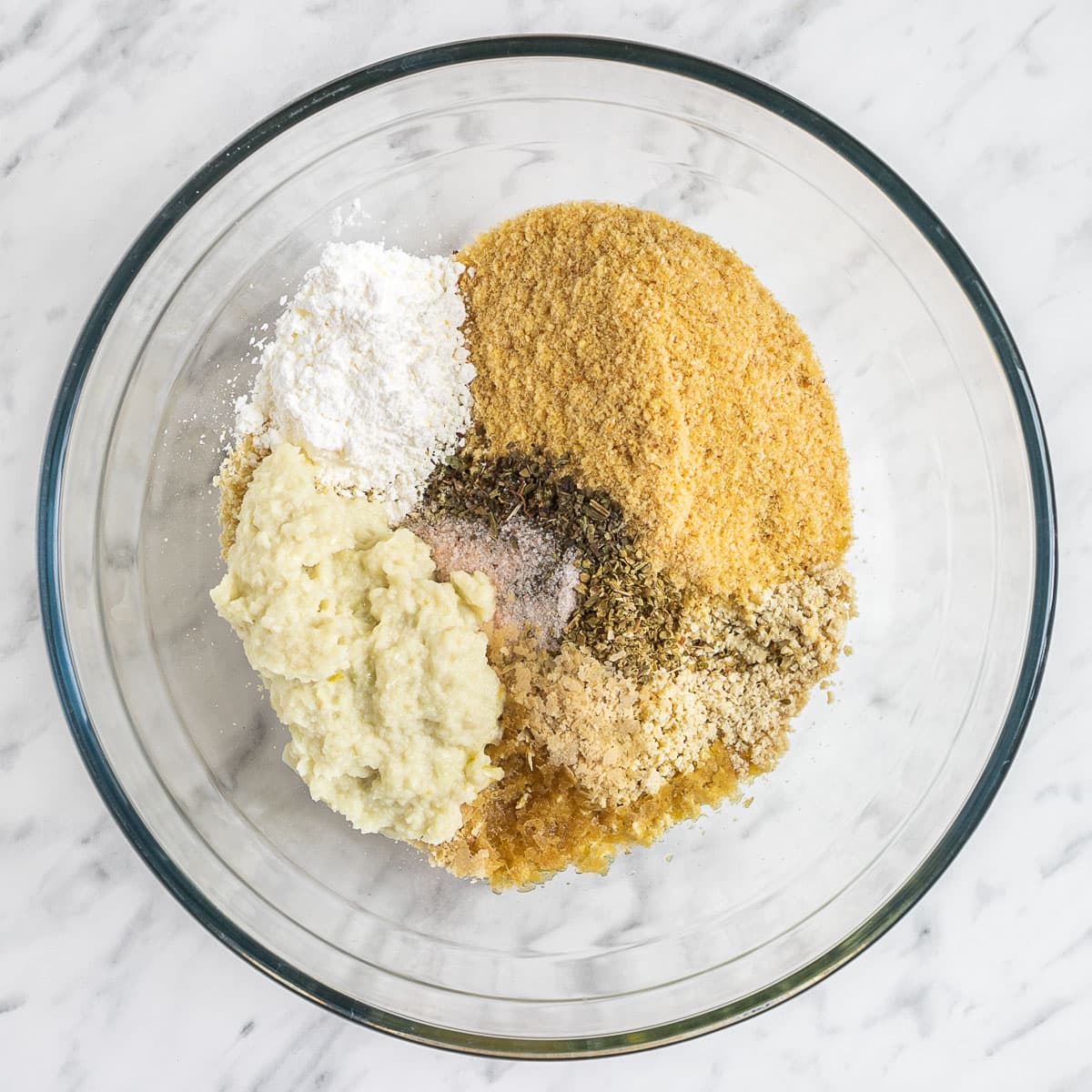 A large glass bowl with different spices and ingredients to make the tofu meatballs.