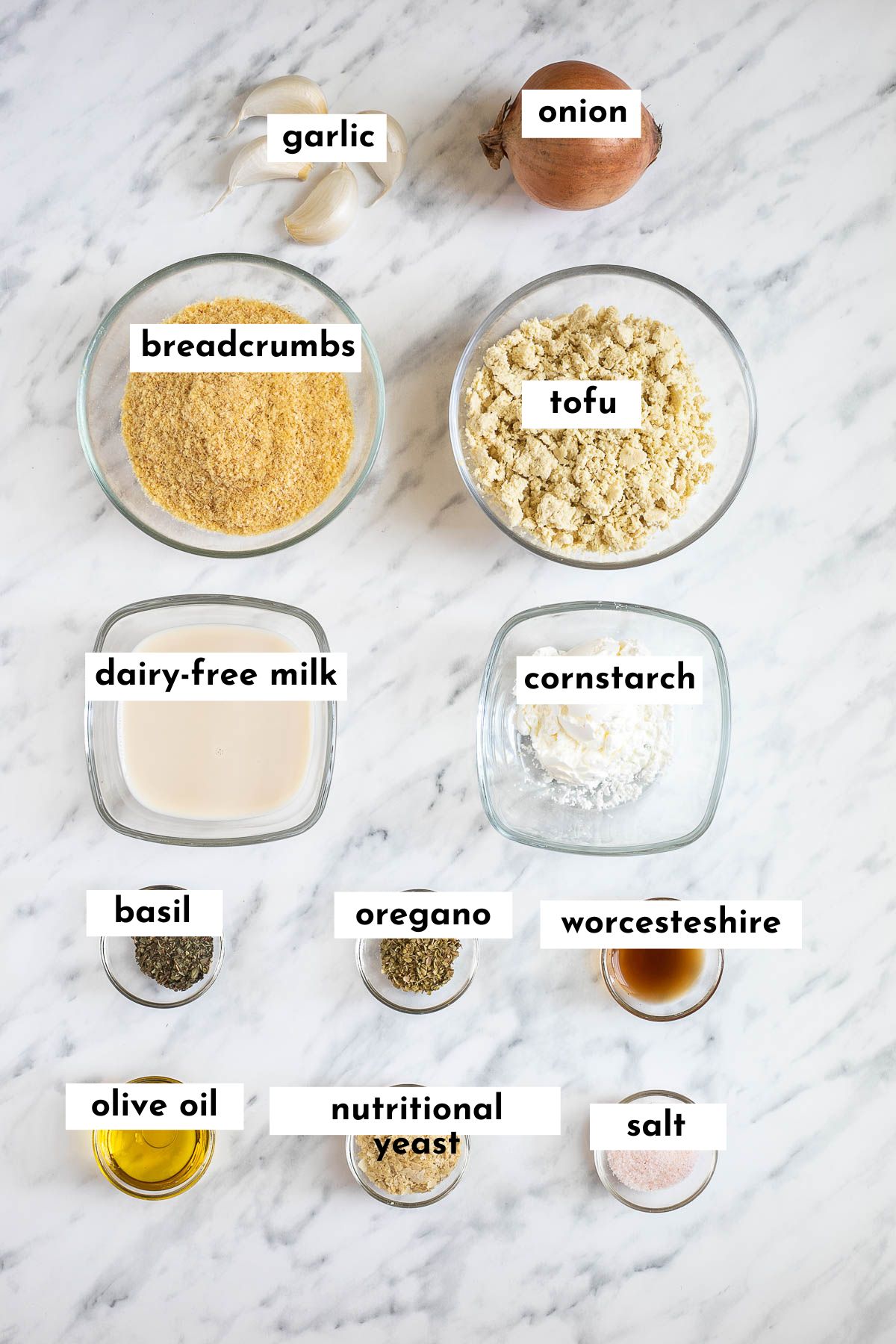 Ingredients of tofu meatballs are placed in small glass bowls like breadcrumbs, tofu mince, milk, garlic, red onion, cornstarch and different spices.
