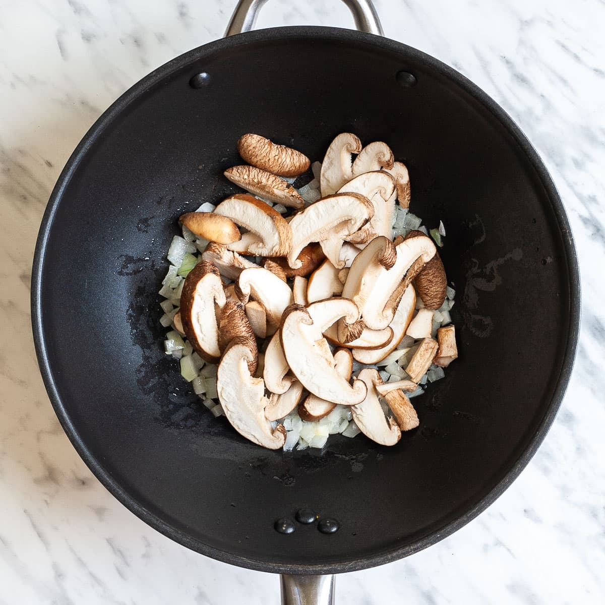 Black wok with sliced mushrooms, chopped onion and garlic.