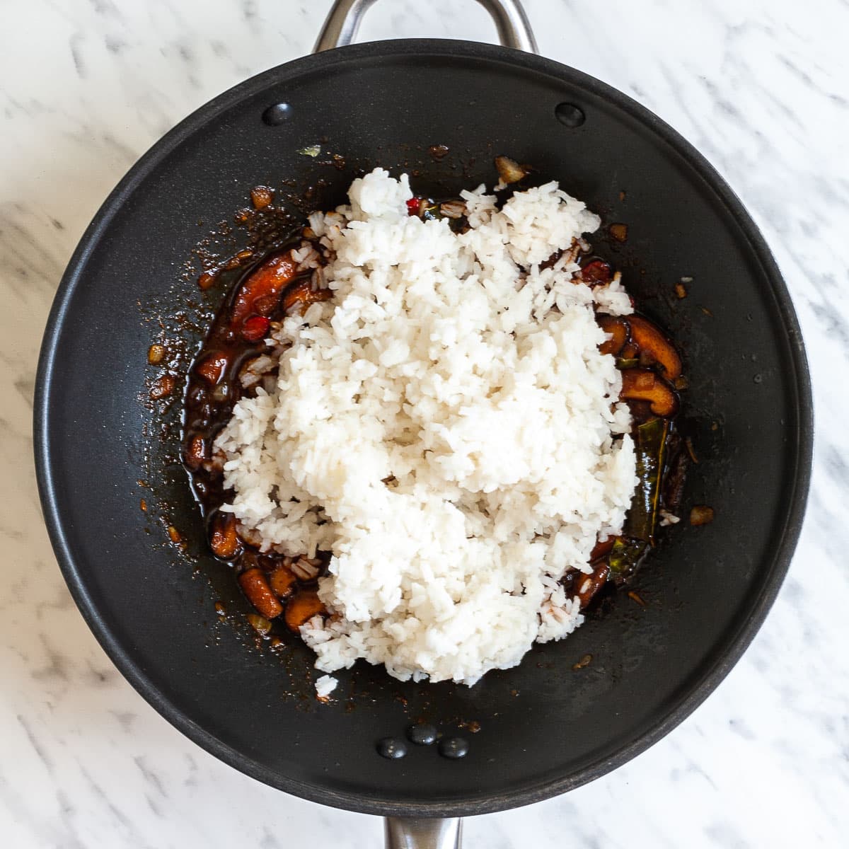 Wok with white rice and a bit of orange brown sauce bit underneath.