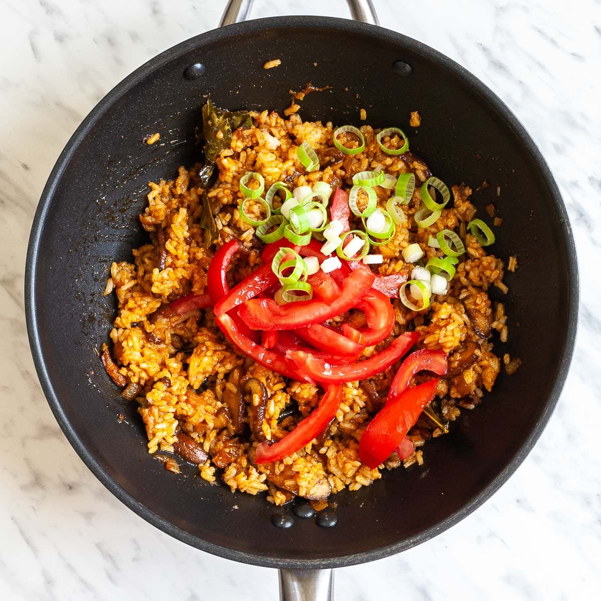 Black wok with orange colored rice topped with sliced tomatoes, and chopped spring onion.