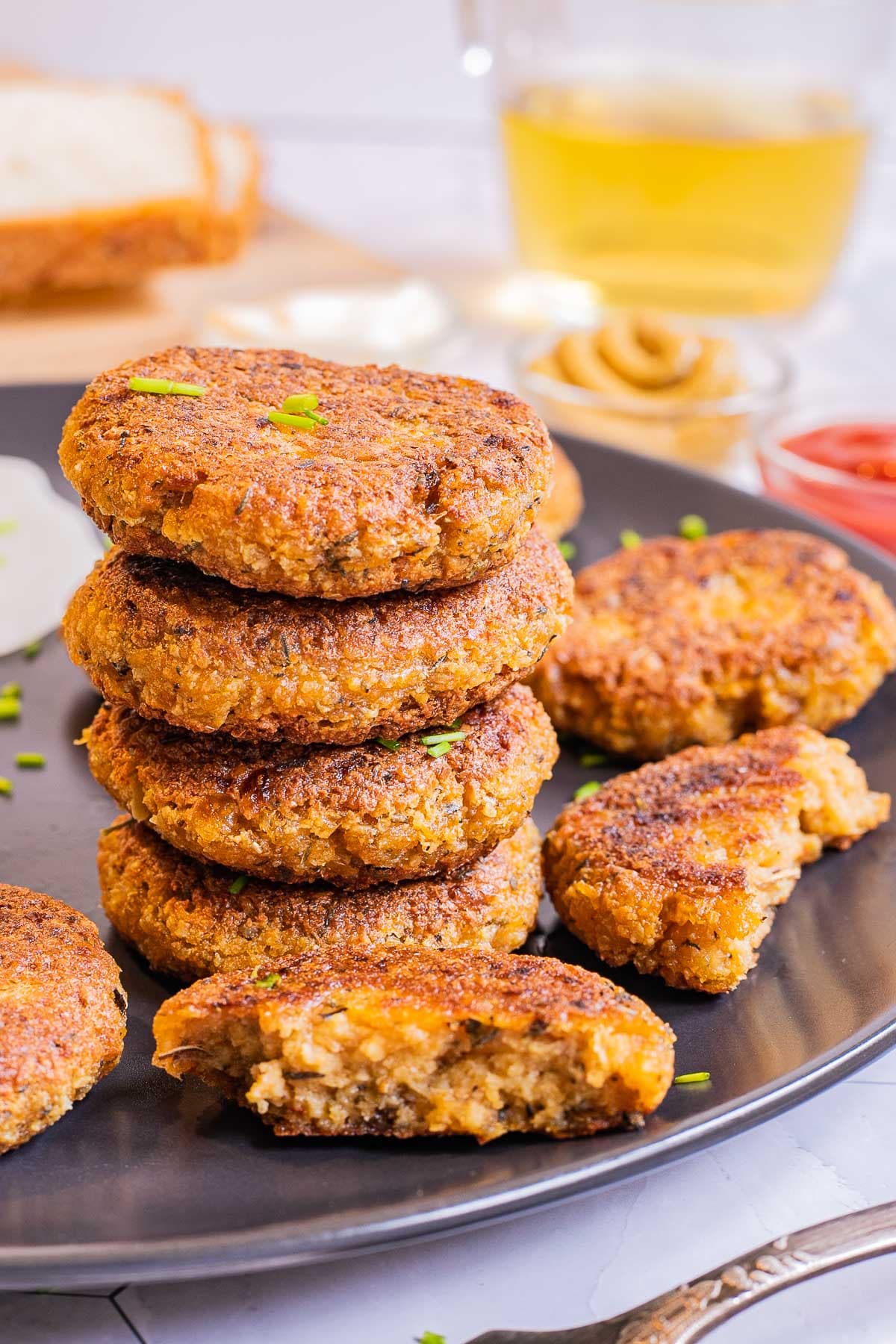 A stack of round flat crispy brown sausage patties on a black plate served with fried egg look-alikes.