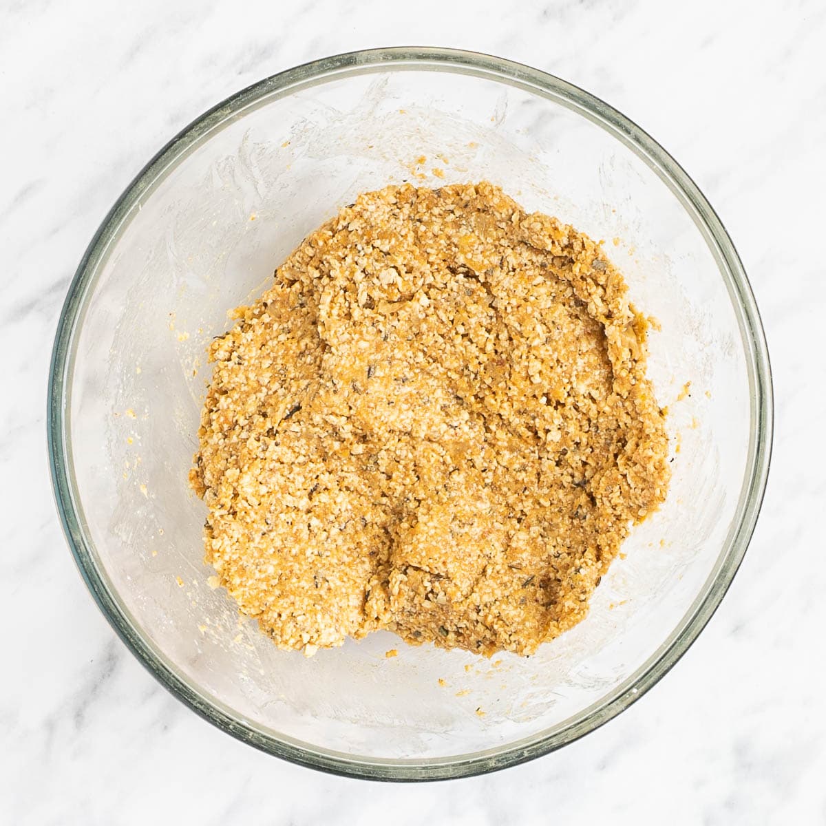 Light brown crumbly dough in a glass bowl to make vegan breakfast sausages.