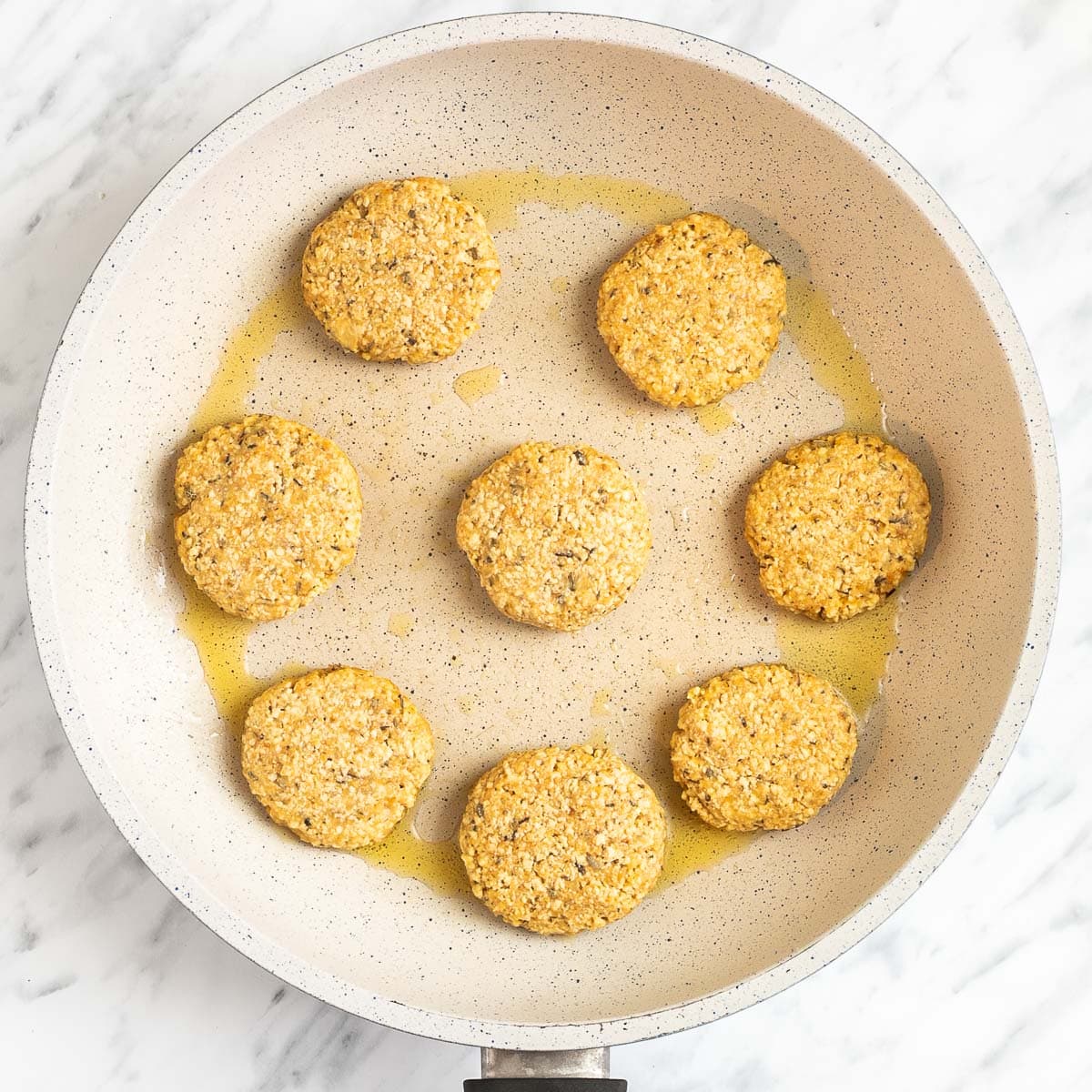 A white frying pan with light brown round sausage patties that are uncooked.