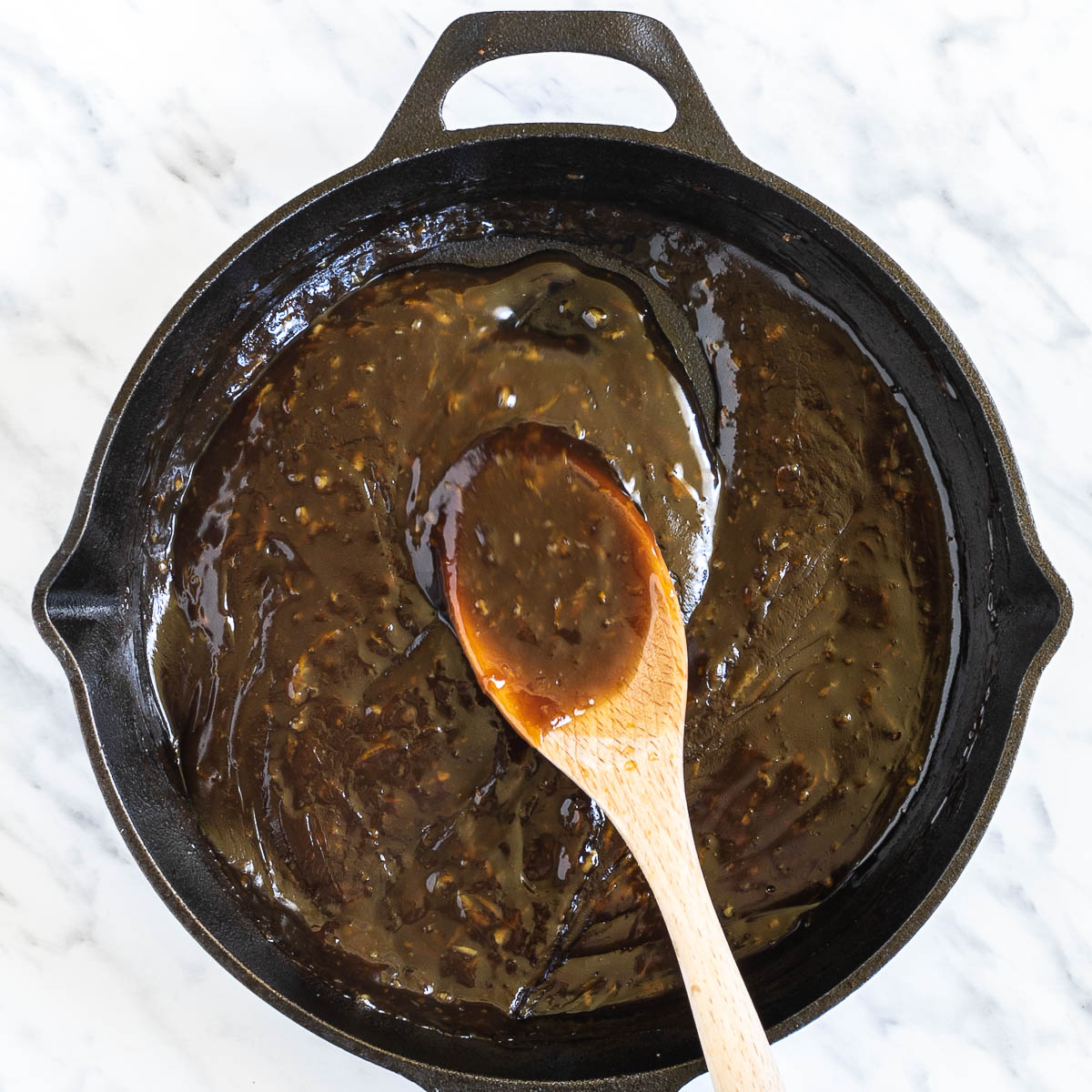 Cast iron skillet with a dark brown thick sauce. A wooden spatula is placed in the middle to show consistency.