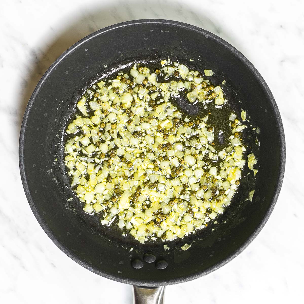 Black frying pan of chopped onion, garlic and whole green peppercorns