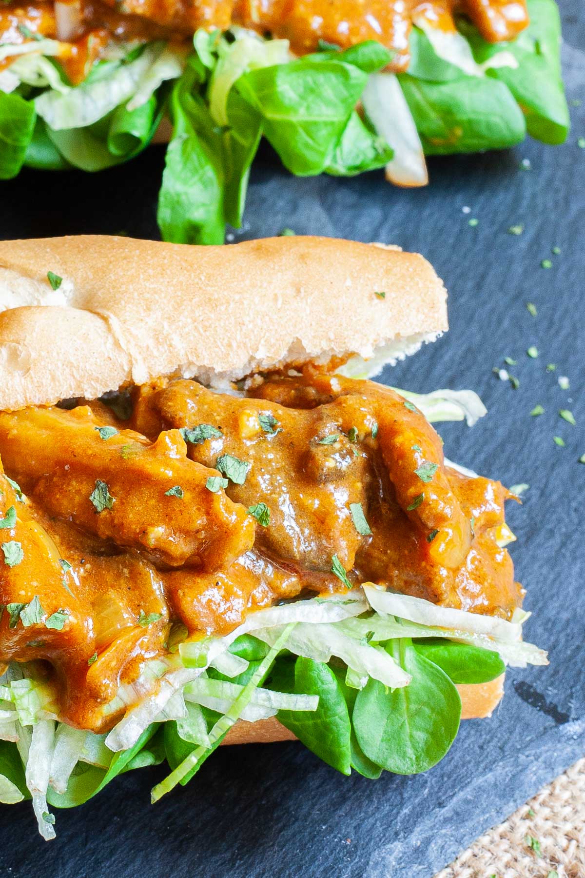 2 hoagie rolls with chopped lettuce and arugula topped with mushroom strips in a brown orange juicy sauce