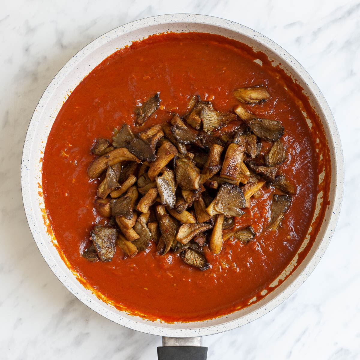 White frying pan with red sauce and brown crispy mushroom strips