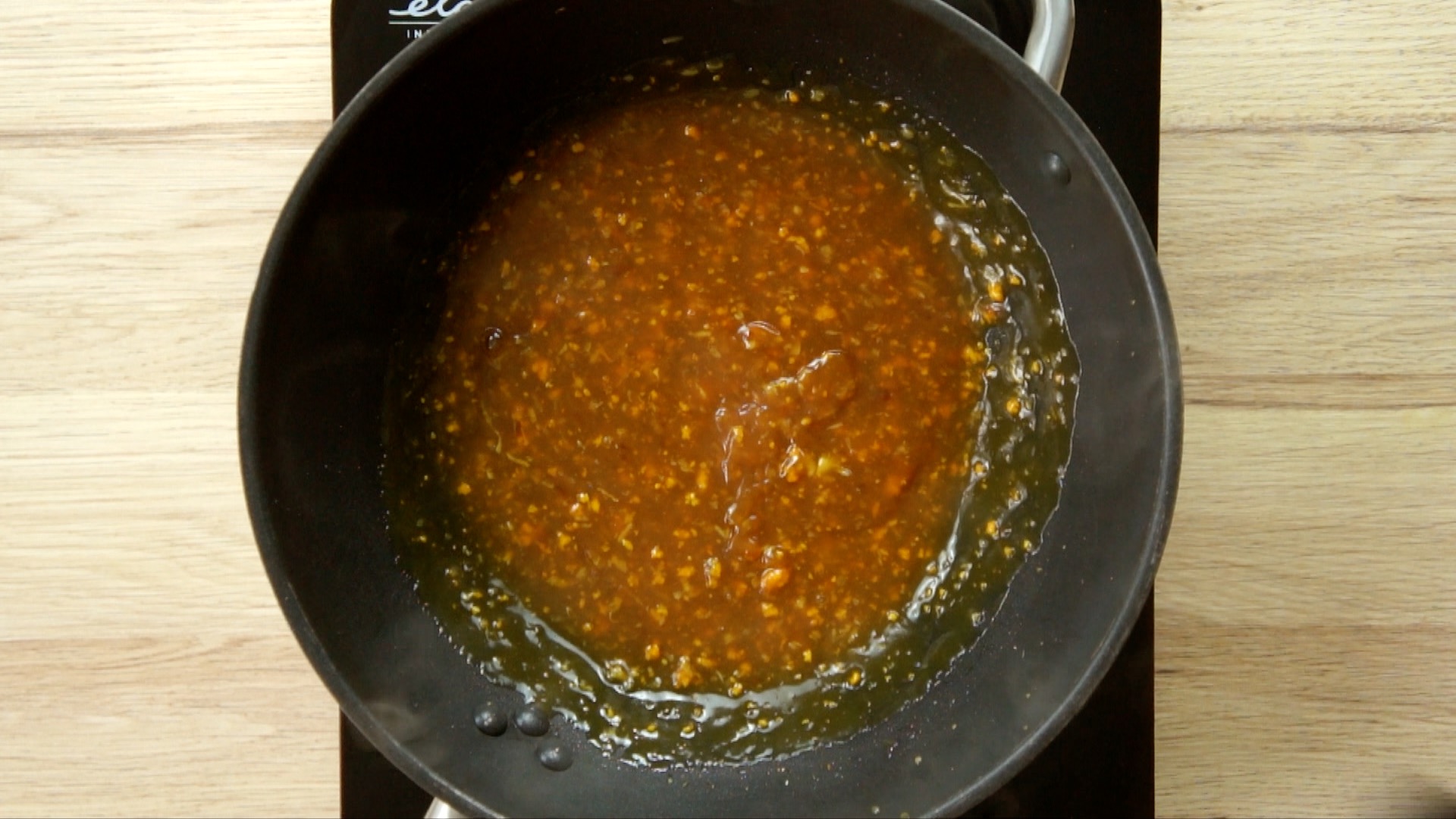 Dark brown sauce with ginger and garlic pieces in a wok.