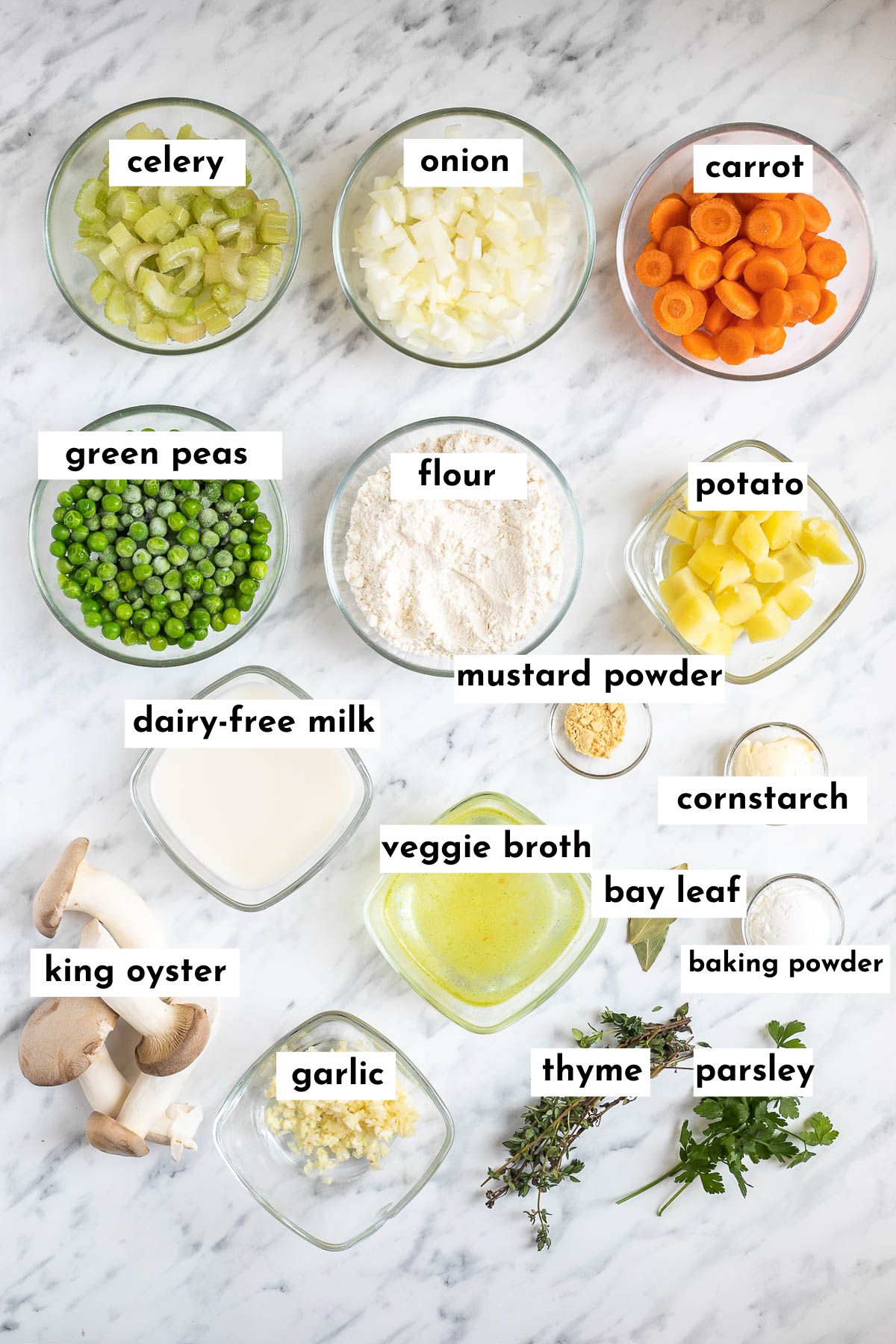 The ingredients and vegan chicken and dumplings is placed in small glass bowls like celery, onion, carrot, green peas, potatoes, flour, milk, broth, oyster mushrooms and different green herbs. 