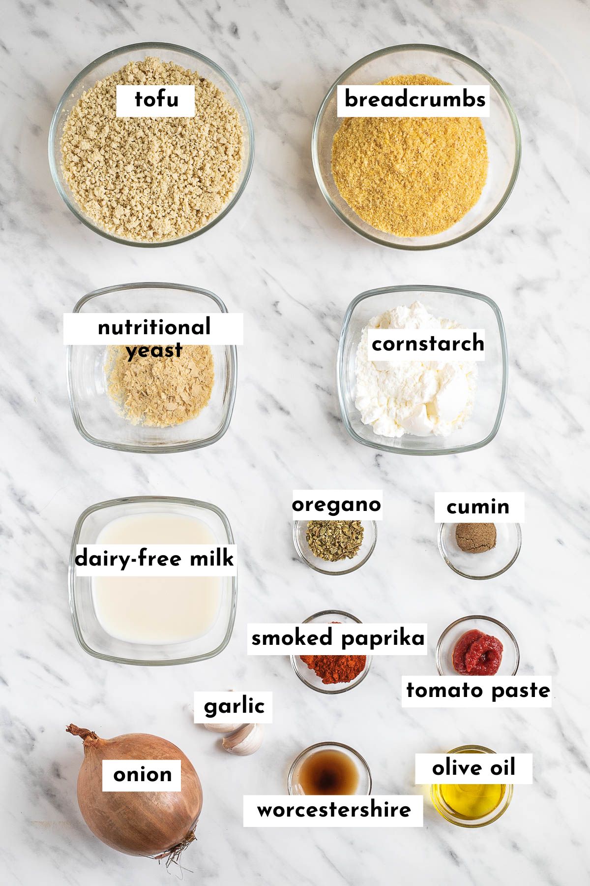 The ingredients of vegan sausage are in small glass bowls minced tofu, breadcrumbs, nutritional yeast, starch, nut milk, onion, garlic clove and 6 different spices.