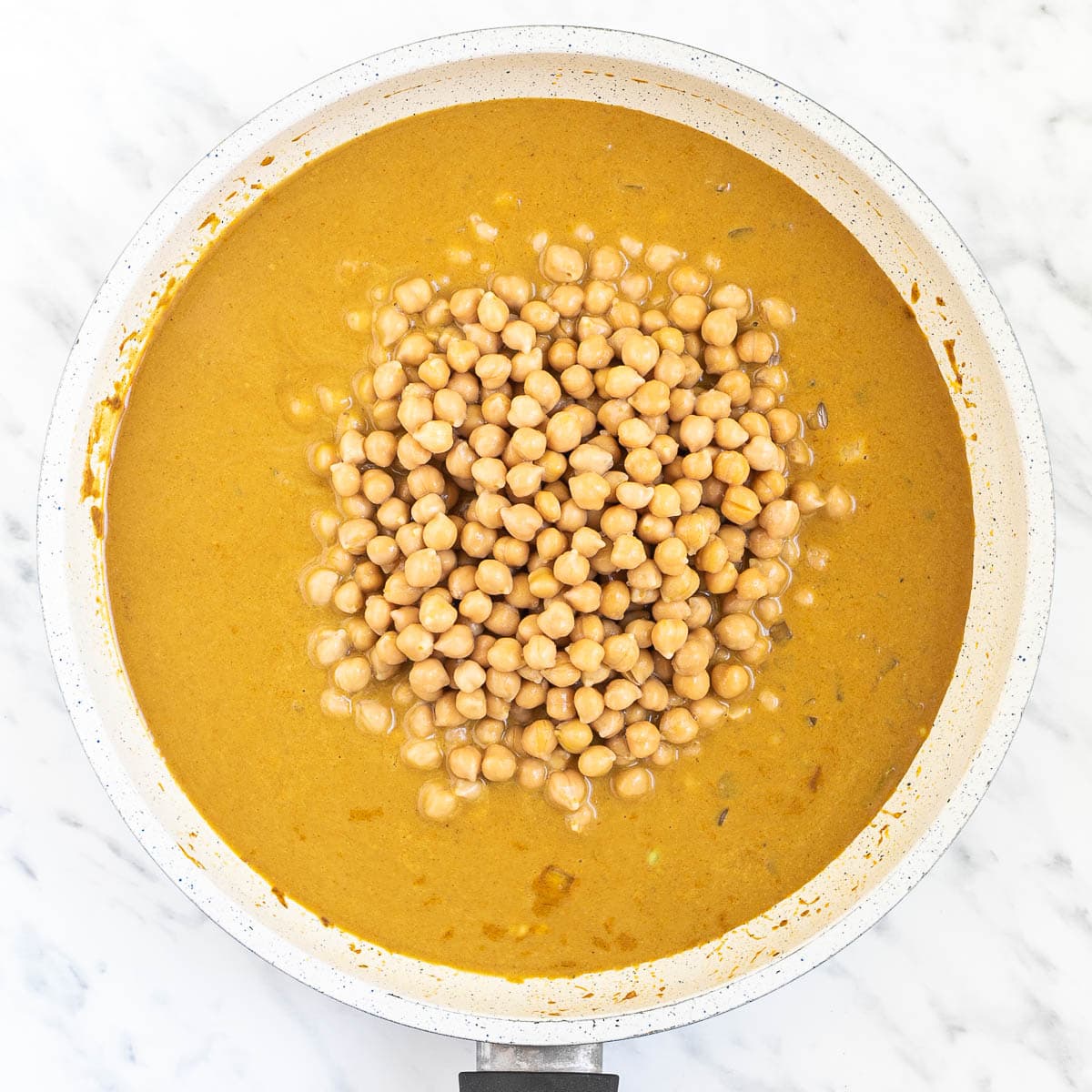 White frying pan with a creamy orange sauce mixed with chickpeas.