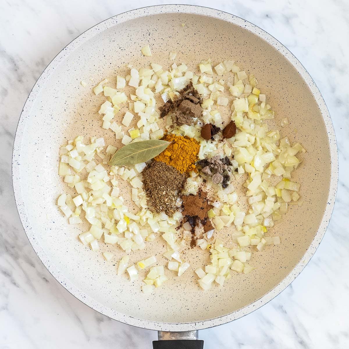 White frying pan with chopped onion, and different colored spices. 