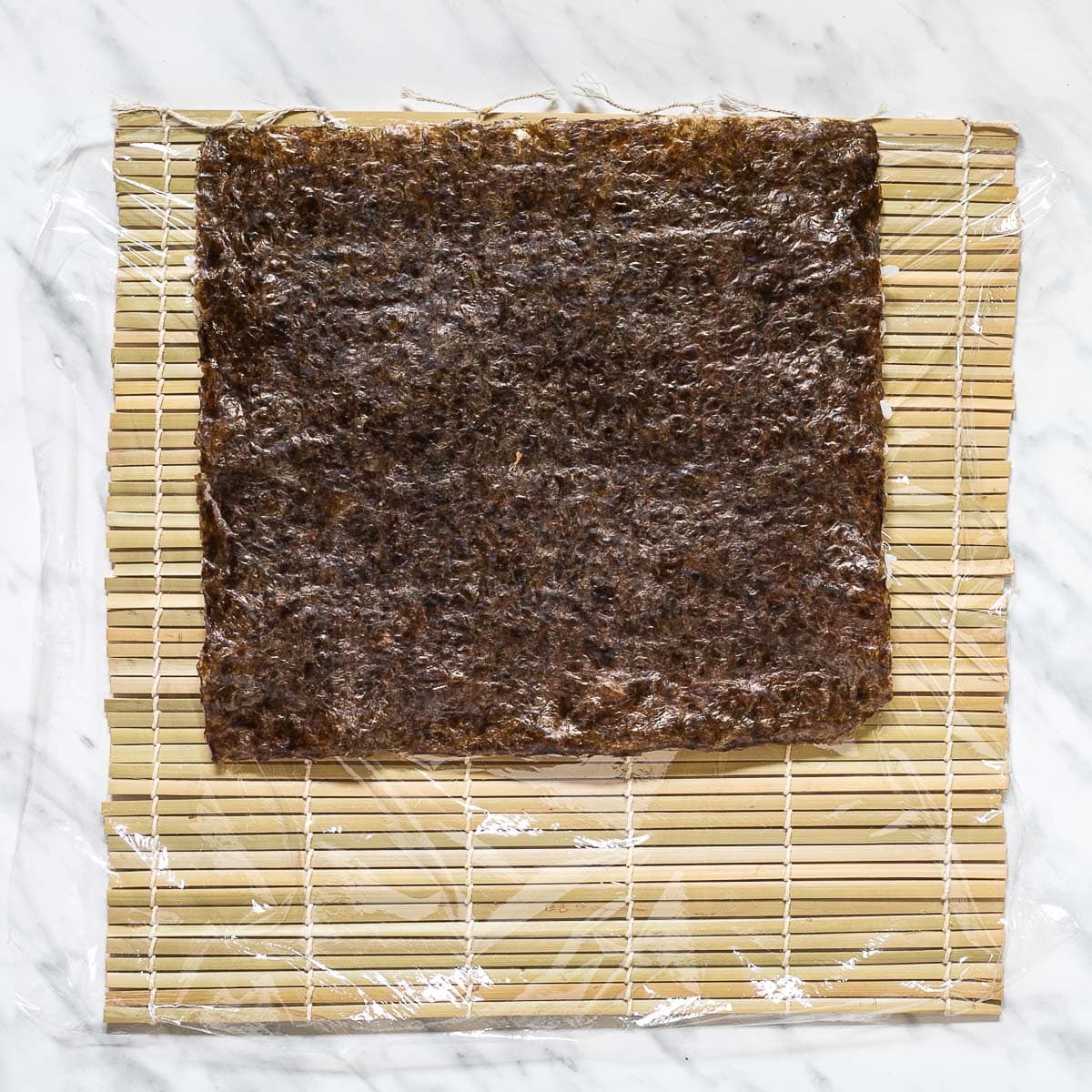 Nori sheets on a bamboo mat covered in plastic wrap.