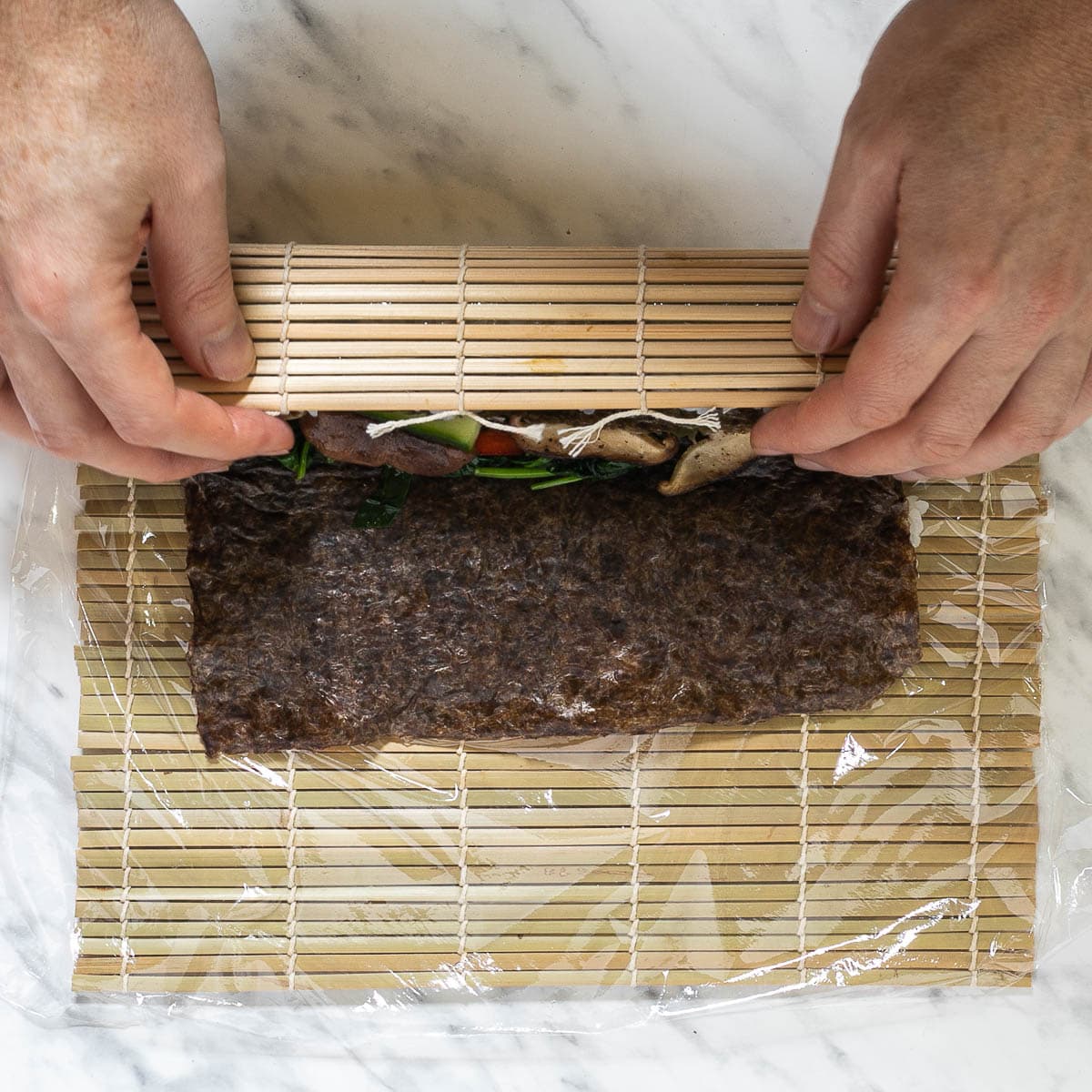 A hand is rolling the sushi using the bamboo mat.
